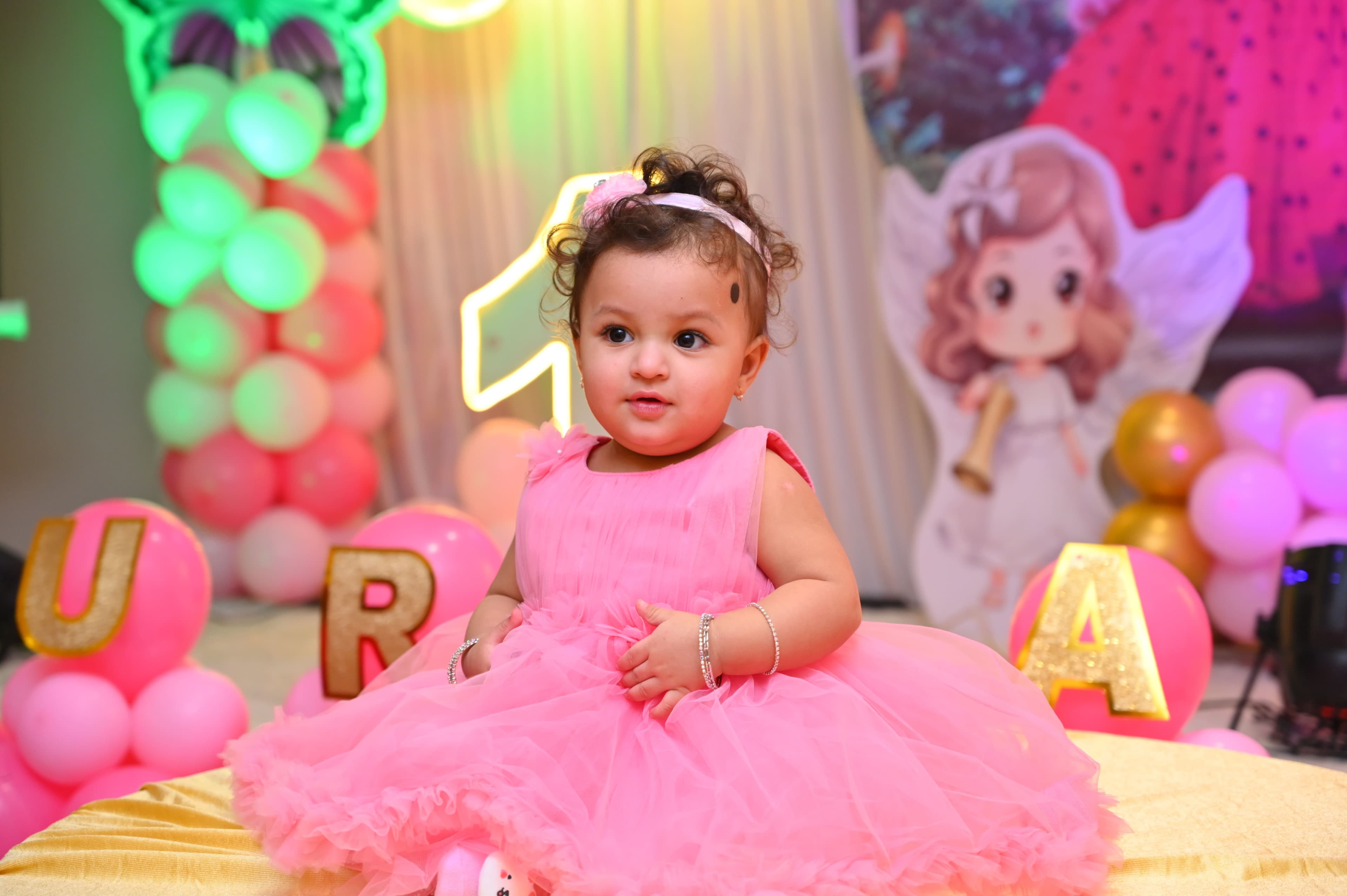 Baby girl in a pink dress with a fairy-themed first birthday backdrop