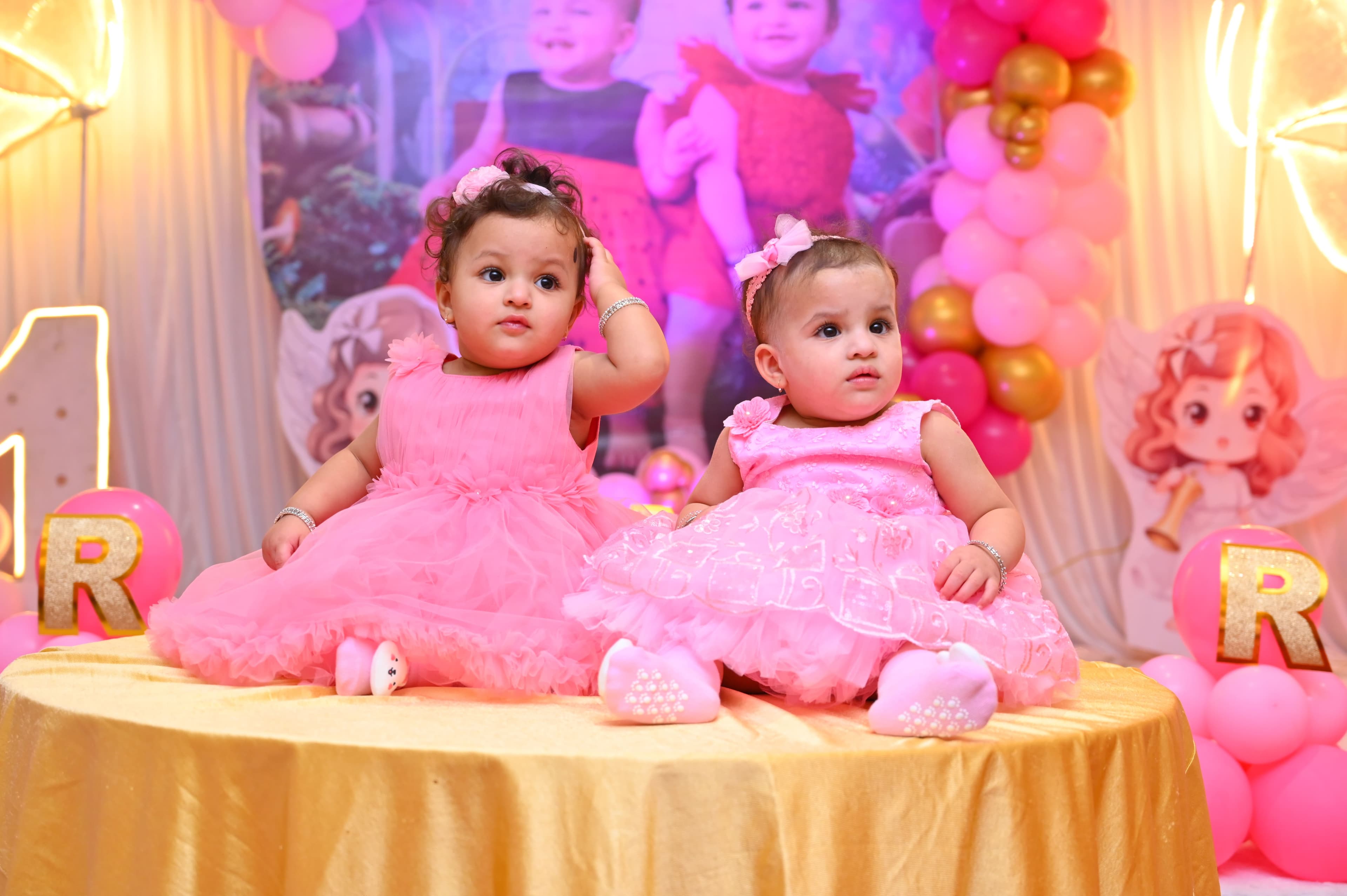 Two baby girls in pink dresses sitting together at their first birthday