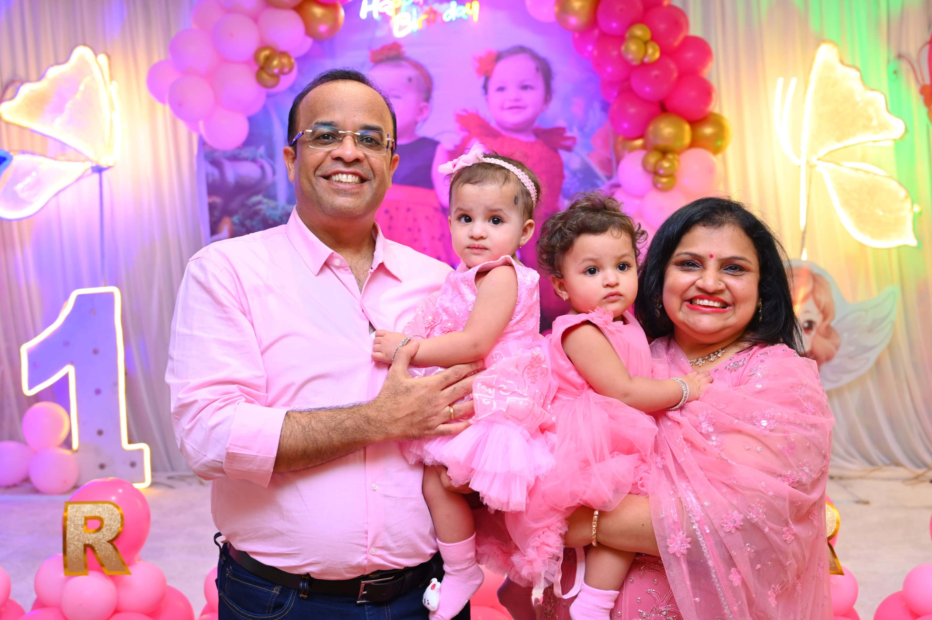 Parents holding their two baby girls at a pink first birthday party