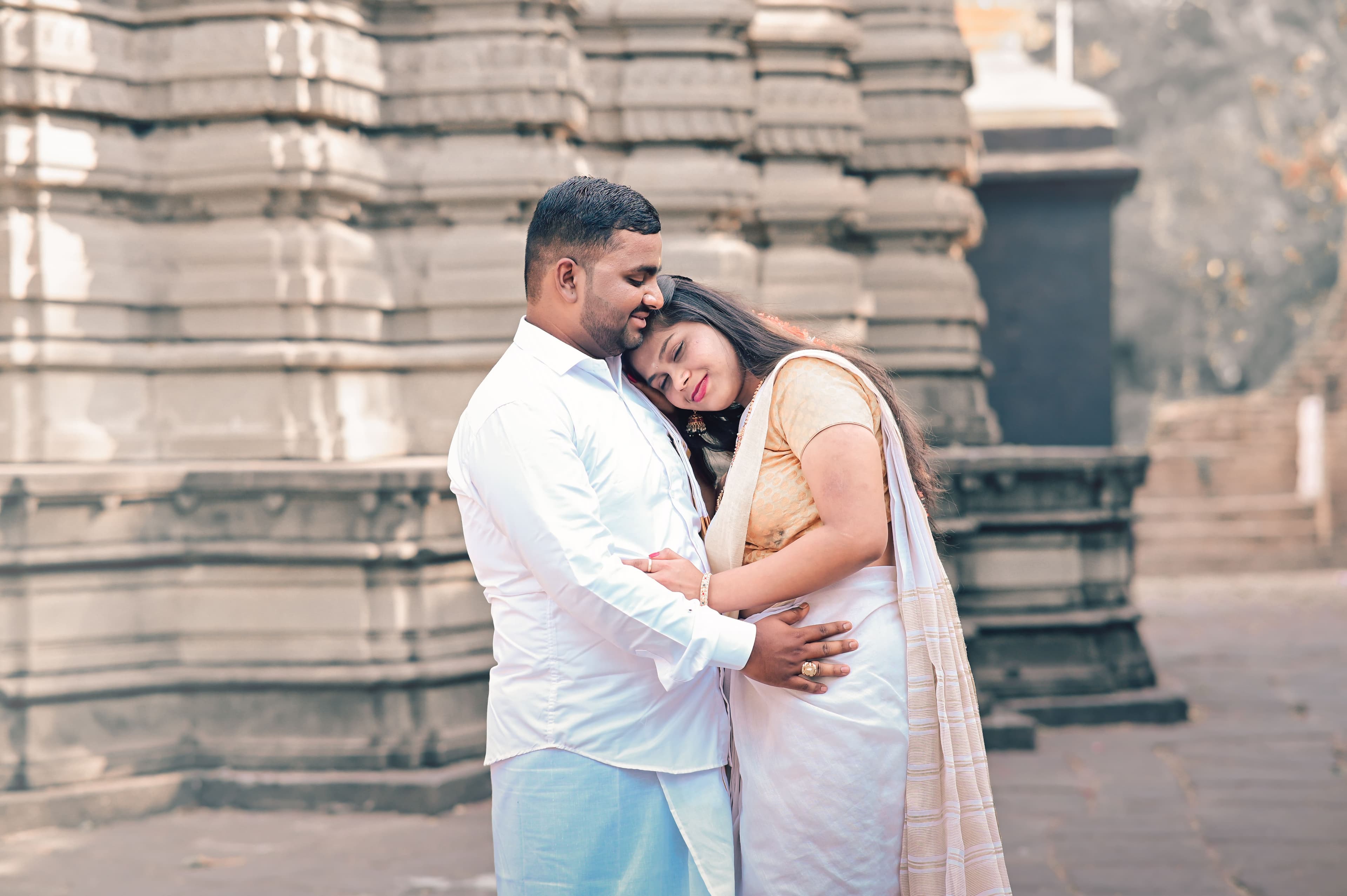 Couple in white traditional outfits embracing at an old stone temple