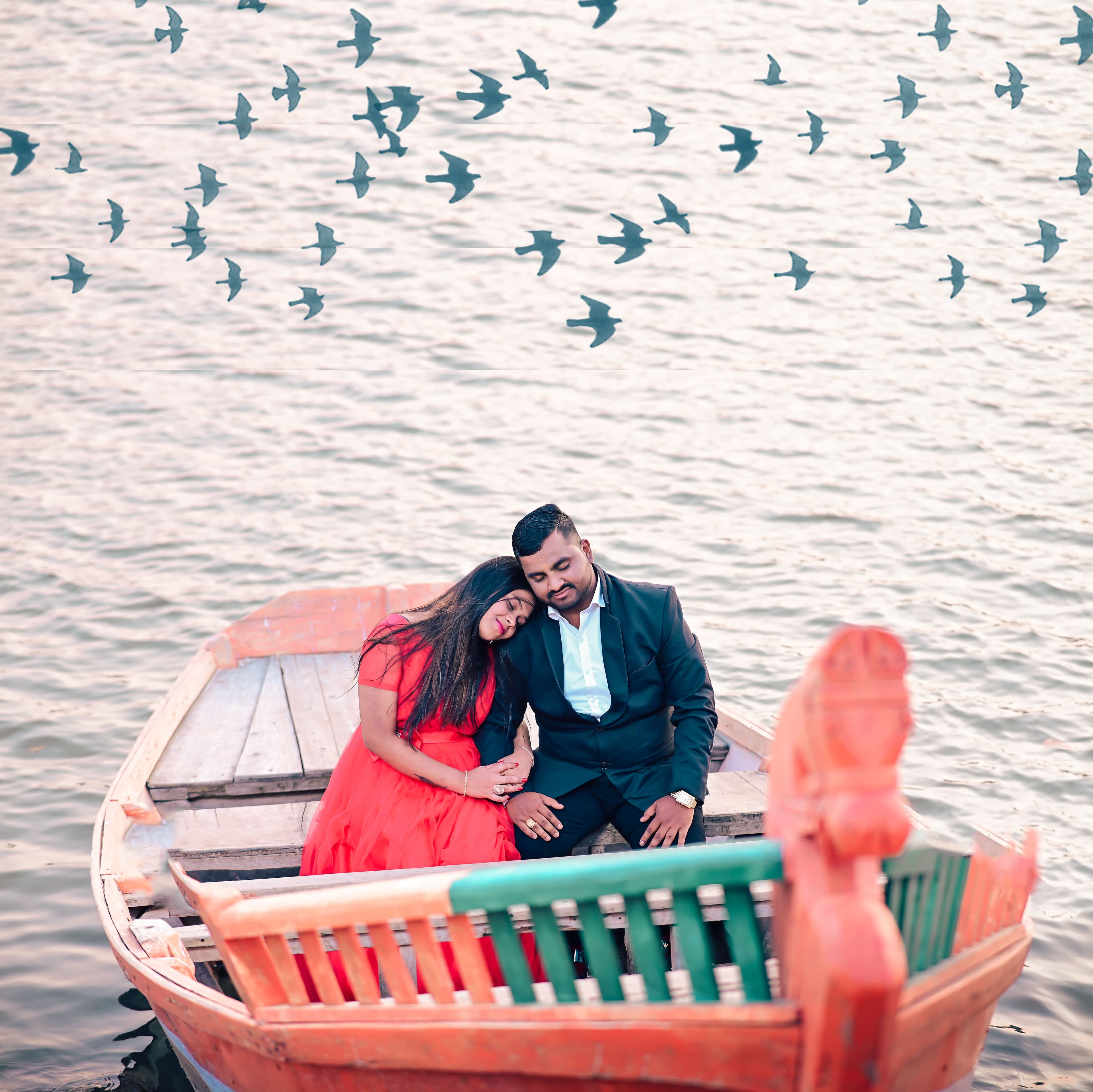Couple sitting in a painted boat on a lake with birds flying overhead