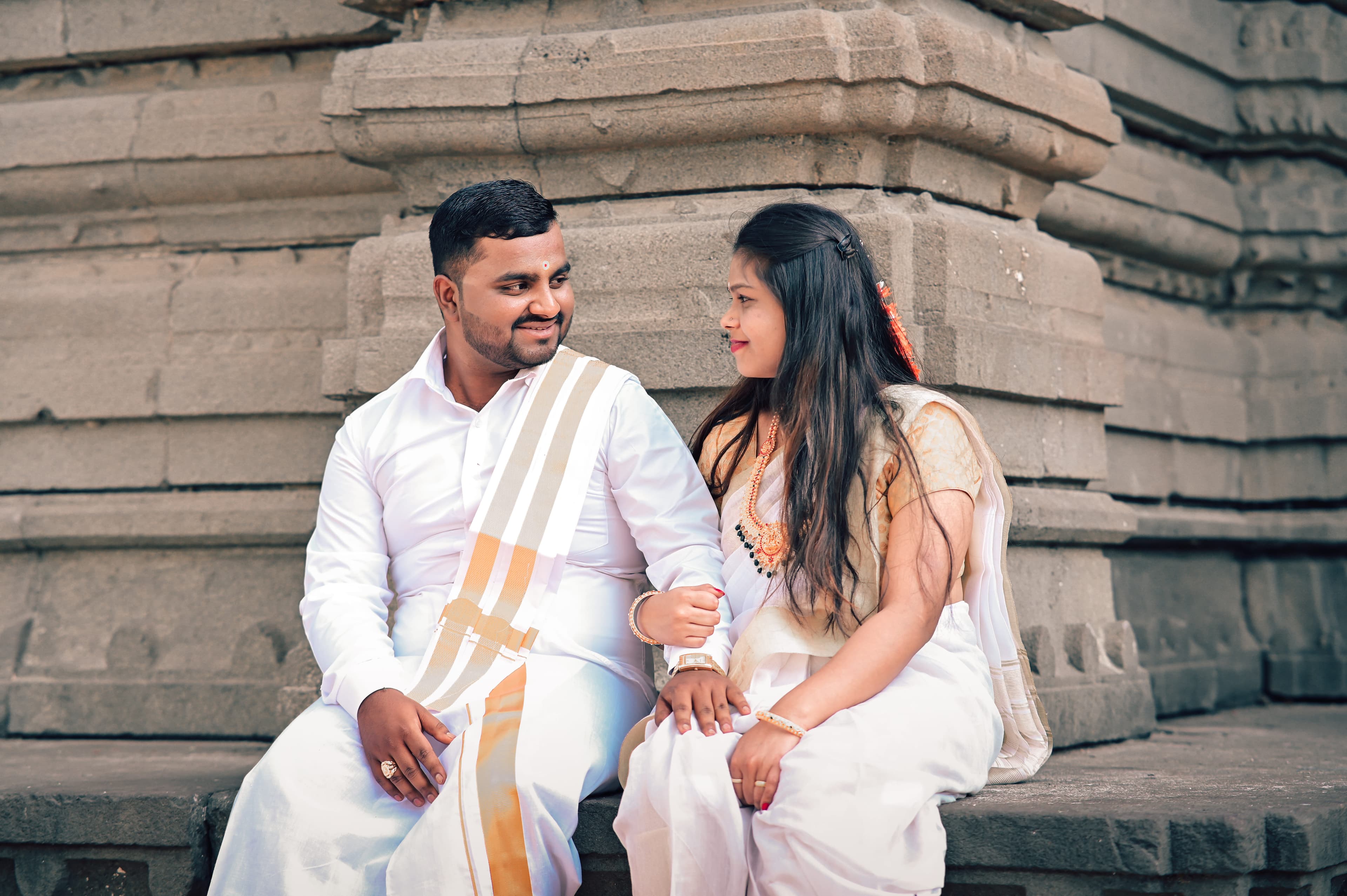 Couple in white traditional outfits laughing on the steps of a stone temple