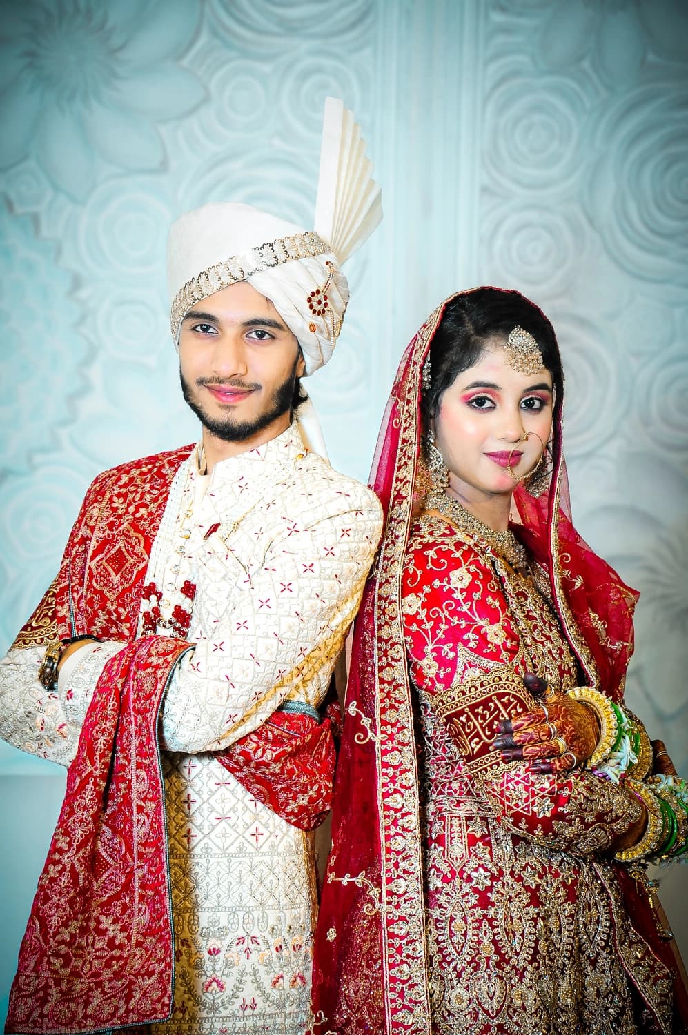 Groom in a sherwani and safa with the bride in a red bridal lehenga, wedding portrait