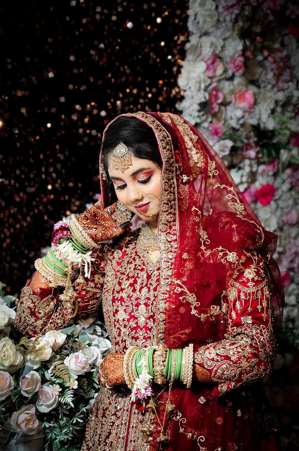 Bride in a red embroidered lehenga and dupatta against a floral backdrop