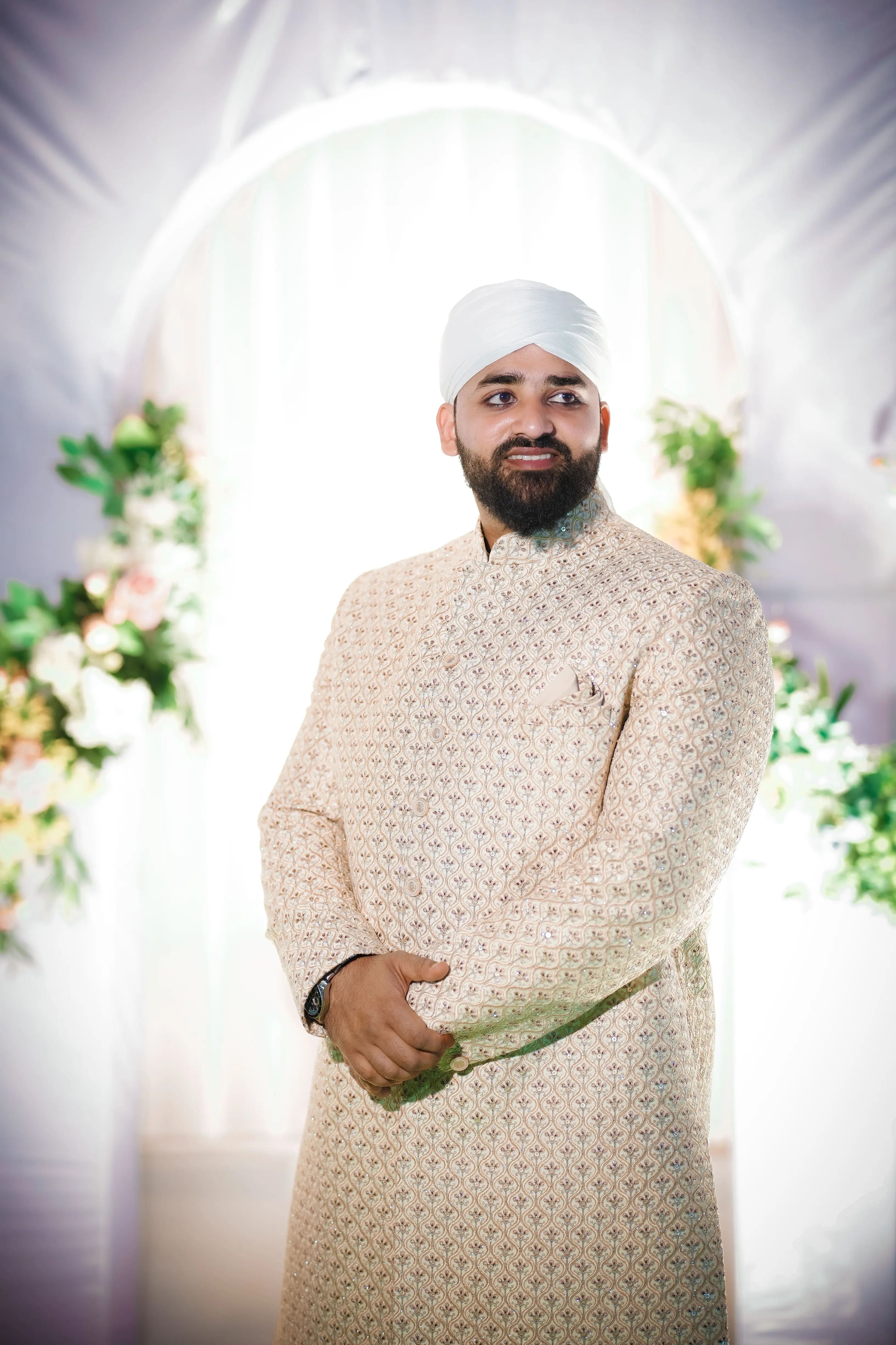 Groom in a cream sherwani and white turban against floral decor