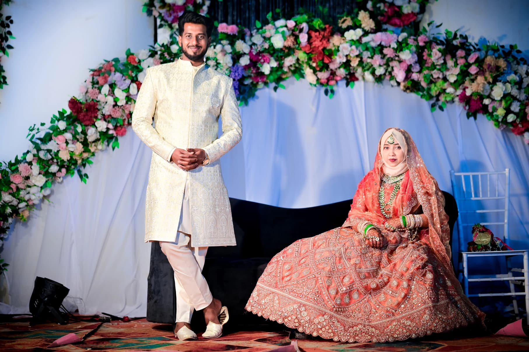 Bride in a red lehenga and groom in a white sherwani on a floral wedding stage